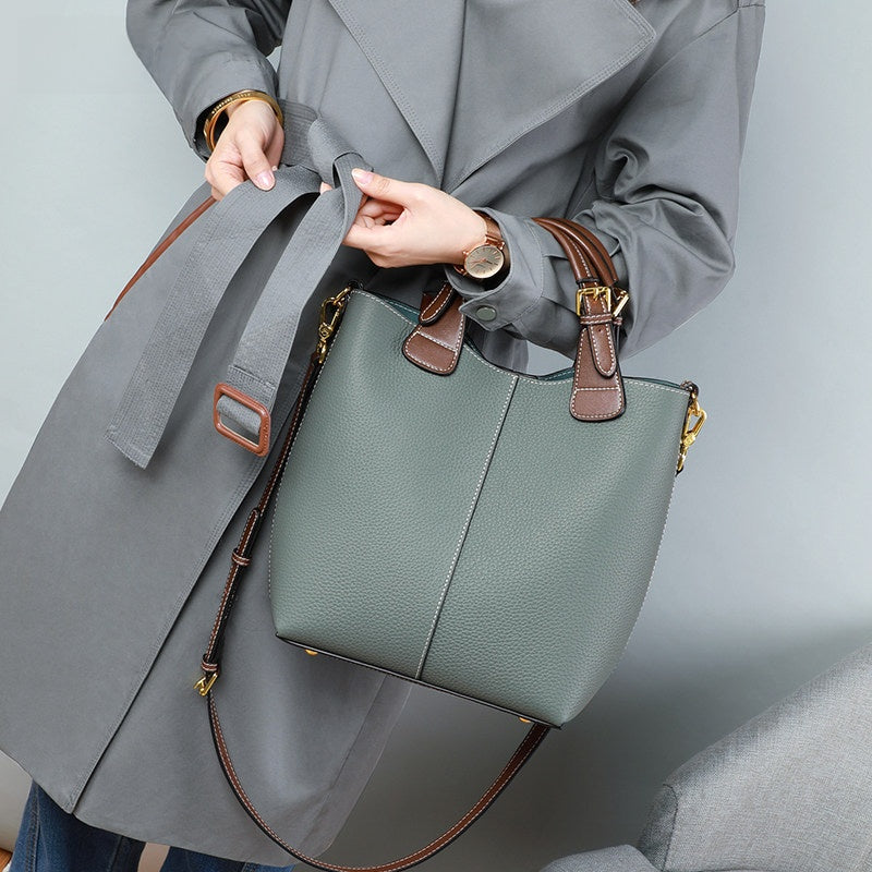 Person holding a green handbag with brown straps against a gray background