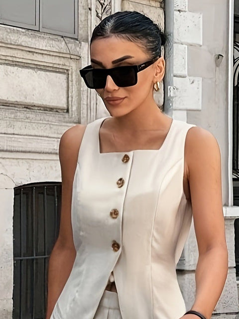 Woman in a beige sleeveless top and pants walking on a city street.