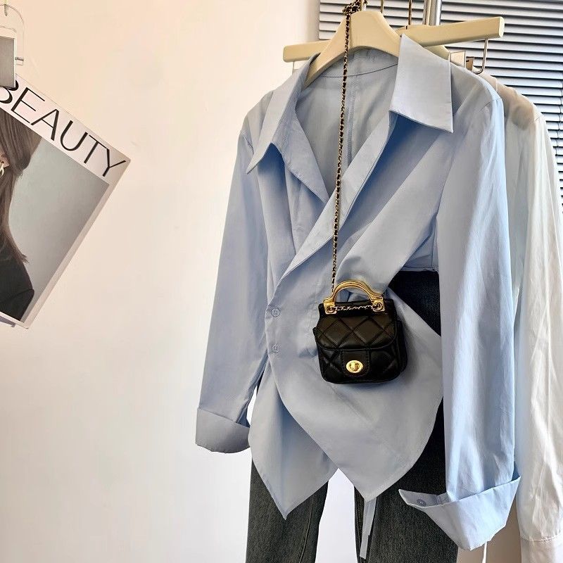 Light blue shirt on a hanger with a black handbag featuring gold chain and clasp.