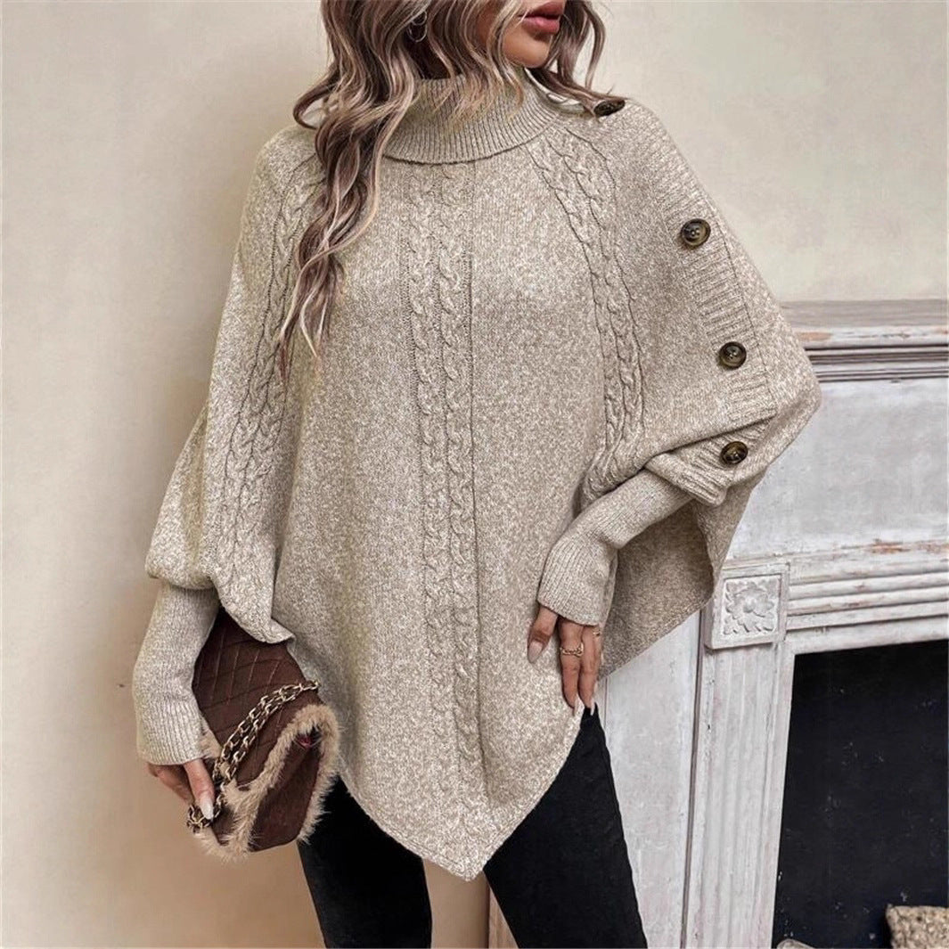 Person wearing a beige cable knit poncho with buttons, holding a brown leather bag.