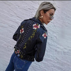 Person wearing a dark blue jacket with floral embroidery against a white brick wall.