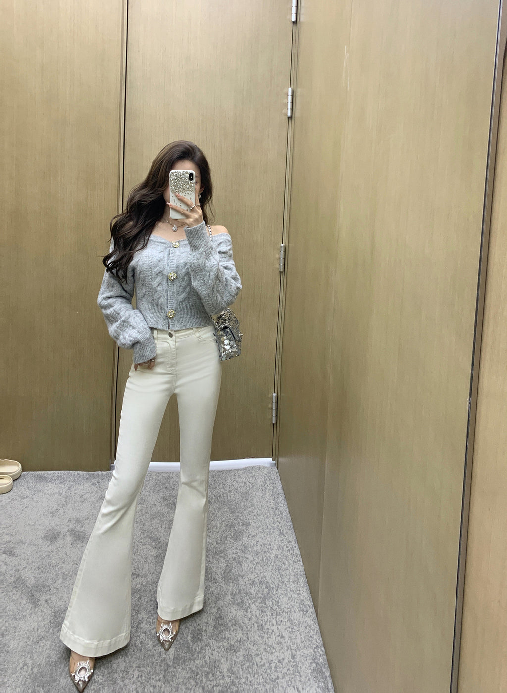 Woman taking a mirror selfie wearing a light blue top and white pants in a fitting room.