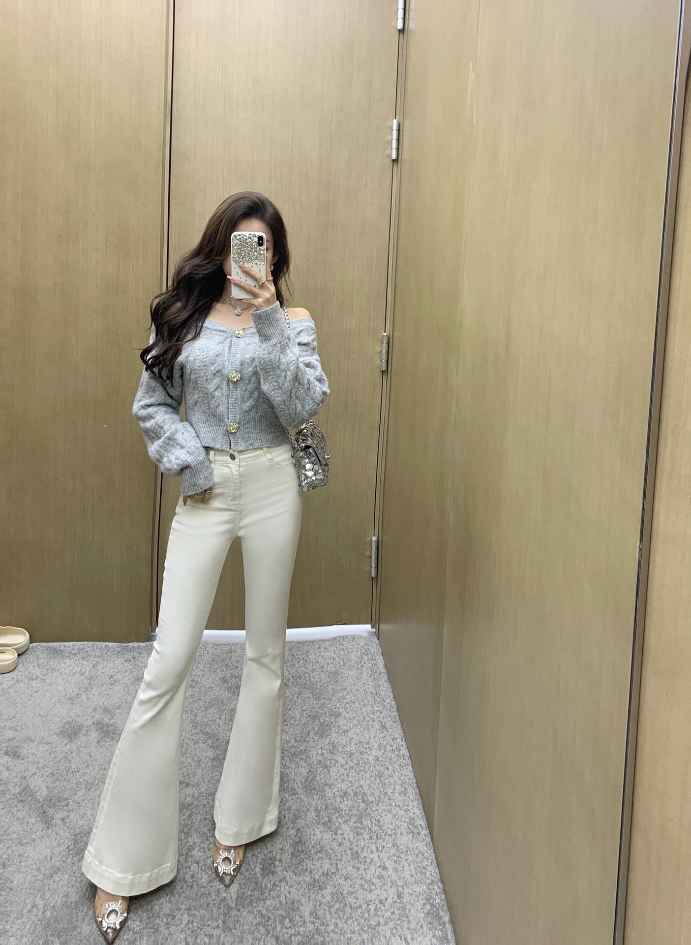 Woman taking a mirror selfie wearing a light blue top and white pants in a fitting room.