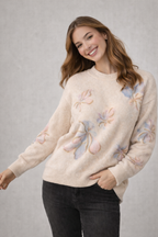 Woman wearing a cream sweater with floral patterns on a gray background