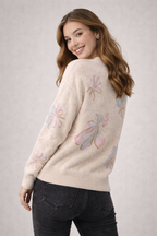 Woman wearing a cream sweater with floral embroidery on a plain background