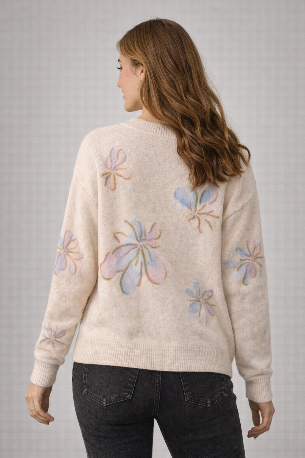 Woman wearing a cream sweater with colorful floral patterns on a gray background