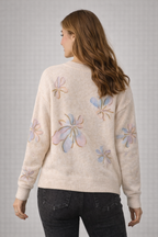 Woman wearing a cream sweater with colorful floral patterns on a gray background