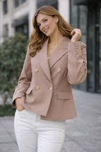 Woman wearing a beige blazer with gold buttons on a city street.