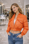 Woman wearing an orange puffer jacket and blue jeans in a shopping mall.