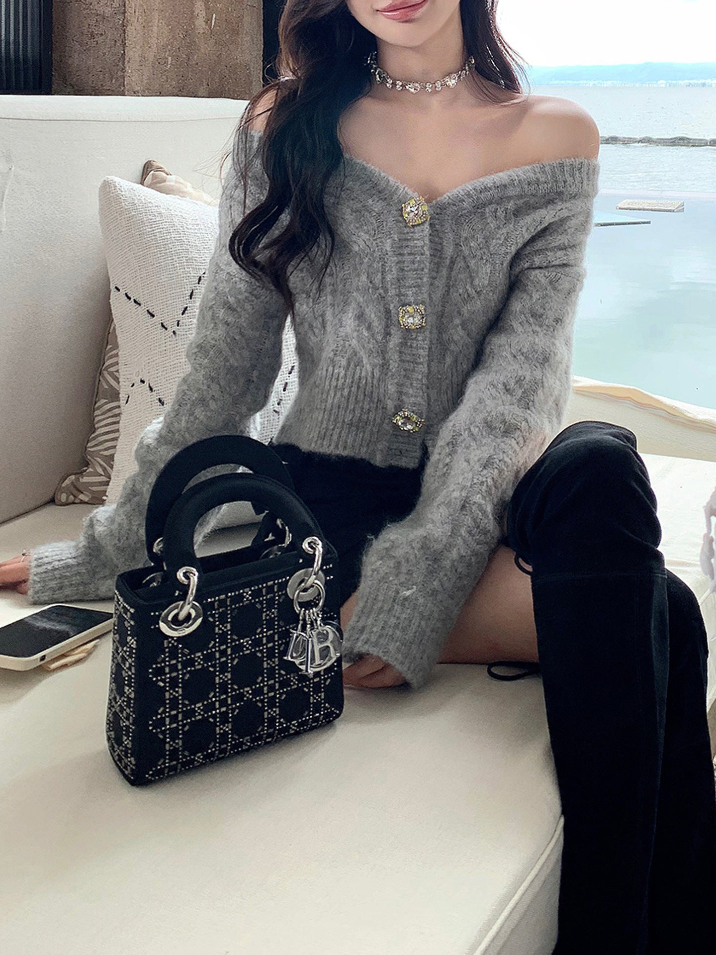 Woman in gray sweater with gold buttons holding a black handbag on a boat.
