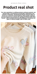 Cream-colored sweater with floral designs on a wooden hanger against a white background.