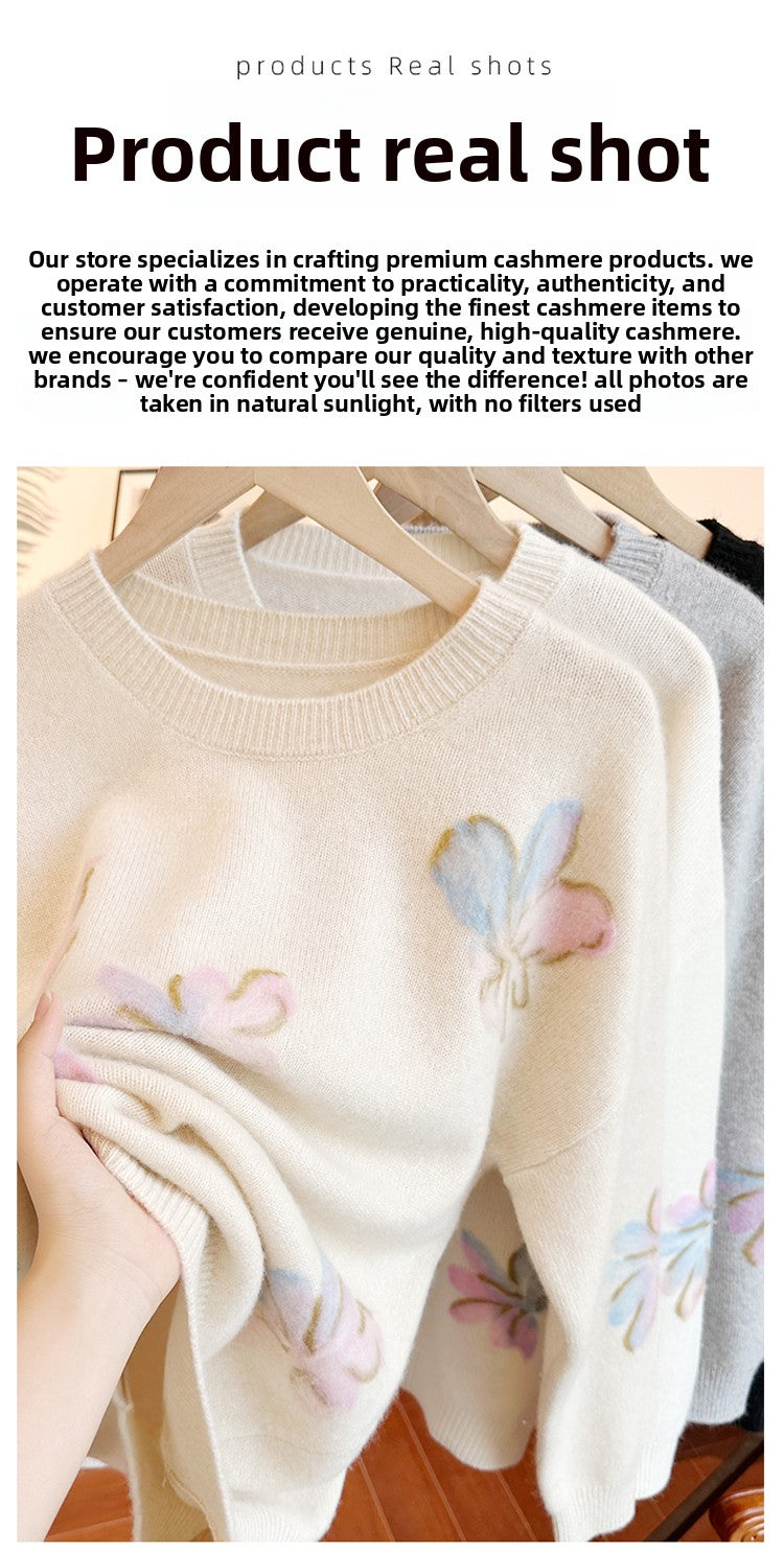 Cream-colored sweater with floral designs on a wooden hanger against a white background.