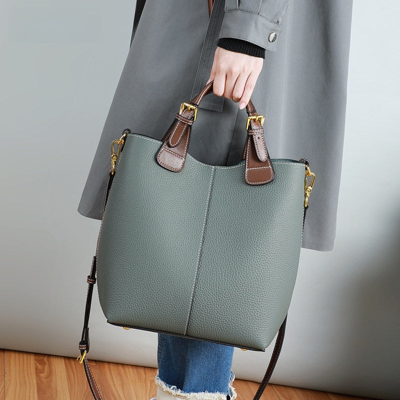 Person holding a green handbag with brown accents against a neutral background