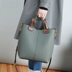 Person holding a green handbag with brown accents against a neutral background
